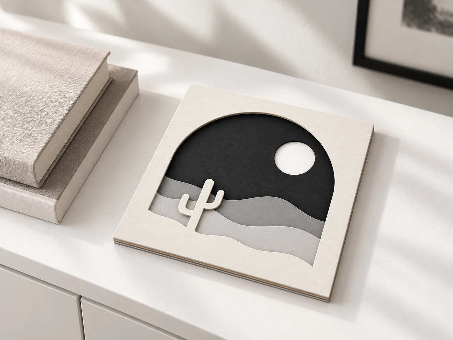 Dune and Sol layered desert artwork with an arch, cactus and circular sun resting on a white console beside books.